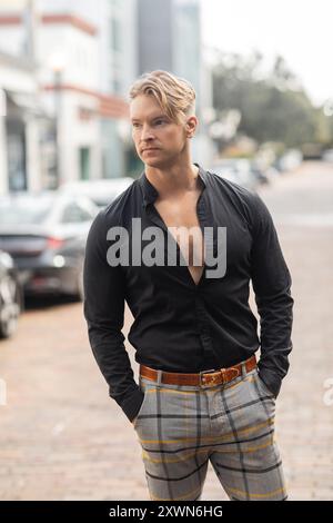 Ein hübscher blonder Mann in einem schwarzen Button-Down-Hemd und karierten Hosen läuft eine Straße in Orlando, Florida. Stockfoto