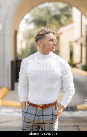 Ein blonder Mann mit weißem Rollkragen und karierter Hose posiert auf einer sonnigen Florida Straße. Stockfoto