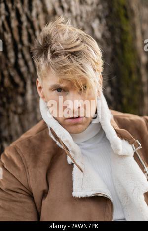 Ein blonder Mann in einer stilvollen braunen Jacke spaziert durch einen grünen Park in Miami. Stockfoto