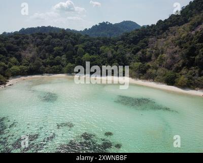 Aus der Vogelperspektive auf einen unberührten Strand auf Koh Ra Wi mit weißem Sand, türkisfarbenem Wasser, Korallenriffen und dichter Vegetation Stockfoto