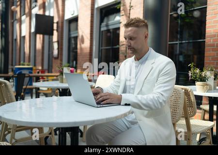 Ein glücklicher, erfolgreicher europäischer Geschäftsmann, der im Freien mit seinem Laptop spricht und lächelt, sitzt im Stadtcafé auf der Straße der Stadt. Stockfoto