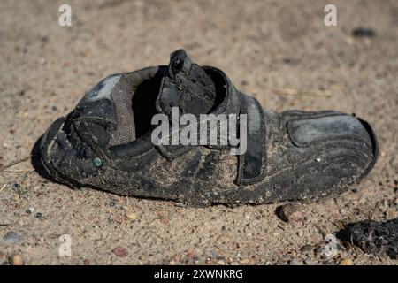 Ein alter, dreckiger, faltiger, schwarzer Schuh, der auf einer Schotterstraße liegt Stockfoto