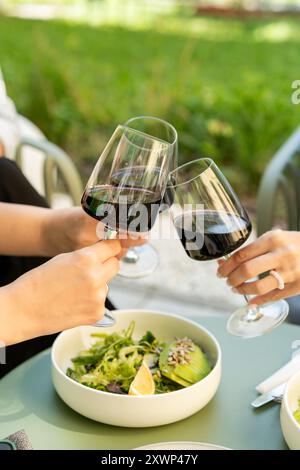 Nahaufnahme von drei Frauen, die im Freien zu Mittag essen und einen feierlichen Toast mit Gläsern Rotwein machen Stockfoto