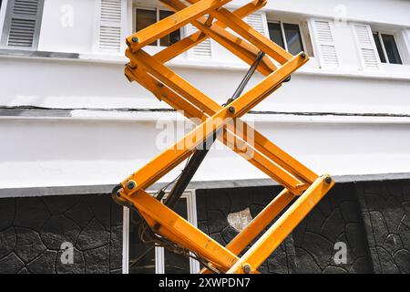 Scherenheber auf dem Dach eines Gebäudes, bereit für Wartungs- oder Bauarbeiten. Eine gelbe und schwarze Leiter wird verwendet, um den zu erreichen Stockfoto