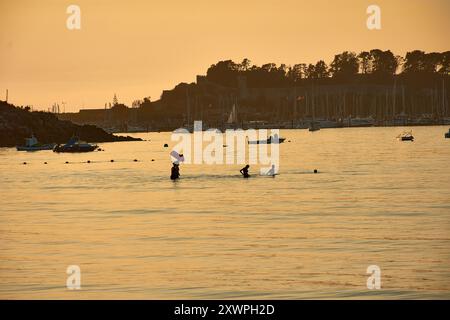 Während der Tag in die Nacht vergeht, schaffen die Silhouetten junger Menschen, die im Wasser des Ladeira Beach spielen und baden, ein fesselndes und nostalgisches erlebnis Stockfoto