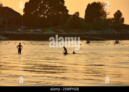 Während der Tag in die Nacht vergeht, schaffen die Silhouetten junger Menschen, die im Wasser des Ladeira Beach spielen und baden, ein fesselndes und nostalgisches erlebnis Stockfoto