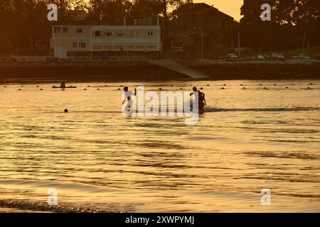 Während der Tag in die Nacht vergeht, schaffen die Silhouetten junger Menschen, die im Wasser des Ladeira Beach spielen und baden, ein fesselndes und nostalgisches erlebnis Stockfoto