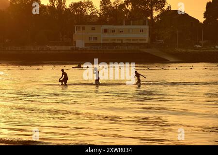 Während der Tag in die Nacht vergeht, schaffen die Silhouetten junger Menschen, die im Wasser des Ladeira Beach spielen und baden, ein fesselndes und nostalgisches erlebnis Stockfoto