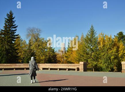 Ein Mädchen in einem warmen Mantel und Hut blickt über einen Herbstpark. Sie wird von hinten fotografiert Stockfoto