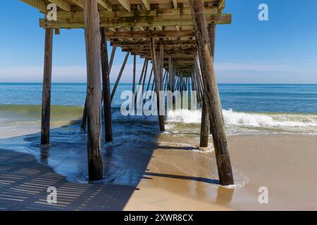 Avon Fishing Pier vier von unten vom Strand, während kleine Wellen vom Atlantischen Ozean hereinRollen. Stockfoto