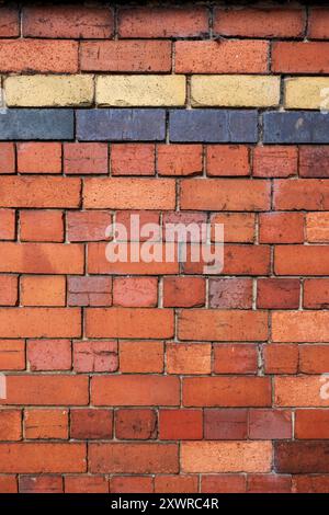 Farbenfrohe Ziegelwand mit verschiedenen Tönen in Rot, Orange, Gelb und Blau. Stockfoto