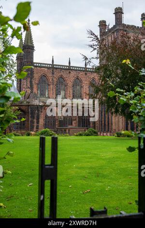 Historische gotische Kathedrale, umgeben von üppigen grünen Gärten und komplizierten Eisenzäunen an einem bewölkten Tag. Stockfoto