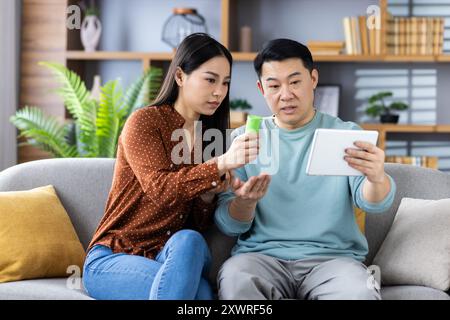 Reifes asiatisches Ehepaar hat sich mit einem Tablet online mit einem Arzt beraten. Mann und Frau schauen aufmerksam auf den Bildschirm, diskutieren Gesundheitsfragen, sitzen zu Hause. Stockfoto