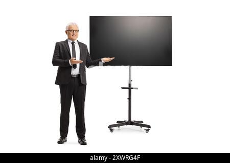 Porträt eines Geschäftsmannes mittleren Alters in voller Länge, der vor einem fernseher auf Ständer isoliert auf weißem Hintergrund präsentiert Stockfoto