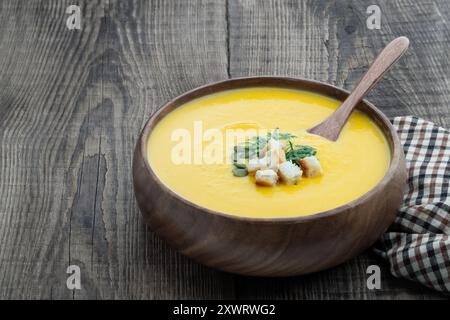Kürbiscremesuppe mit Croutons in einer Holzschale auf rustikalem Tisch Stockfoto