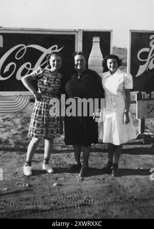 Drei Frauen posieren vor einer Coca Cola Plakatwand in Texas, 1938. Stockfoto