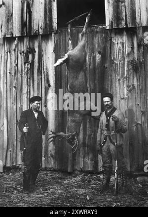 Zwei erfolgreiche Jäger posieren mit einem sehr großen Weissschwanzhirsch, ca. 1910. Stockfoto