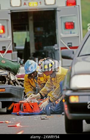 Ersthelfer Rettungskräfte leisten medizinische Hilfe für Opfer bei einem Fahrzeugunfall, während der Verkehr in der Nähe weiter fließt. Stockfoto