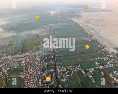 Erleben Sie den Zauber des alten Ägyptens, während farbenfrohe Heißluftballons anmutig über den Nil und die Wüstenlandschaften von Luxors Theben schweben. Stockfoto