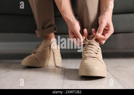 Mann, der drinnen einen Schnürsenkel auf dem Sofa bindet, Nahaufnahme Stockfoto