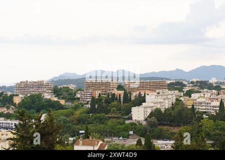 An einem bewölkten Sommertag wird eine Stadt am Hügel von oben betrachtet, mit weißen Gebäuden, die von einem üppigen grünen Baldachin umgeben sind. Stockfoto