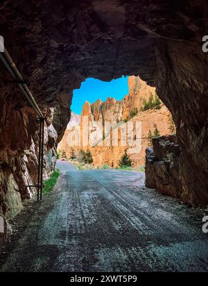 Im Tunnel mit Blick auf den Eingang sehen Sie zerklüftete Klippen und Berge mit Orangetönen vor klarem blauem Himmel. Diese alte Straße öffnet einen Sommertag im Jahr. Stockfoto