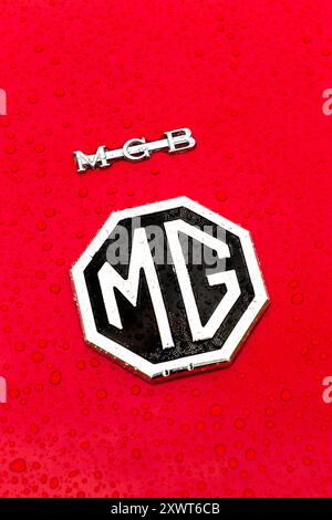 Nahaufnahme des MG-Logos auf einem roten Auto mit Wassertropfen auf der Oberfläche. MGB Stockfoto