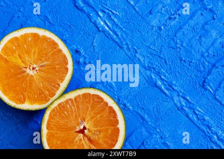 Zwei Teile einer Orange in diagonaler Position in der unteren linken Ecke auf einem blauen Tisch. Stockfoto