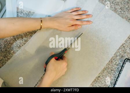 Legen Sie ein Backblech mit Backpapier aus, und schneiden Sie die Rolle mit einer Schere ab. Hochwertige Fotos Stockfoto