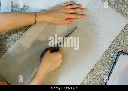 Legen Sie ein Backblech mit Backpapier aus, und schneiden Sie die Rolle mit einer Schere ab. Hochwertige Fotos Stockfoto