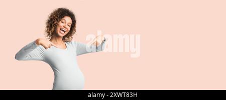 Emotional schwangere Frau lächelt und zeigt mit den Fingern auf den Bauch Stockfoto