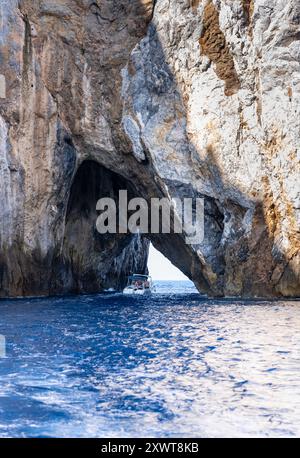 Ein Boot fährt durch einen felsigen Bogen bei Pan di Zucchero, einer Insel in der Nähe von Masua, Sardinien. Dieser berühmte Ort in der Nähe von Porto Flavia ist ein Highlight für die Natur Stockfoto
