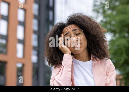 Porträt einer jungen Frau in einer städtischen Umgebung, die Kopfschmerzen hat, Unbehagen und Stress zeigt, während sie ihren Kopf hält. Stockfoto