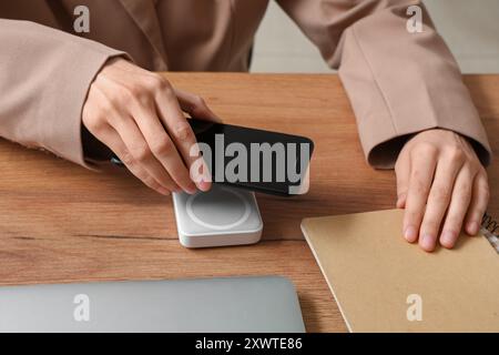 Frau, die modernes Handy auf ein drahtloses Ladegerät auf Holztisch legt, Nahaufnahme Stockfoto