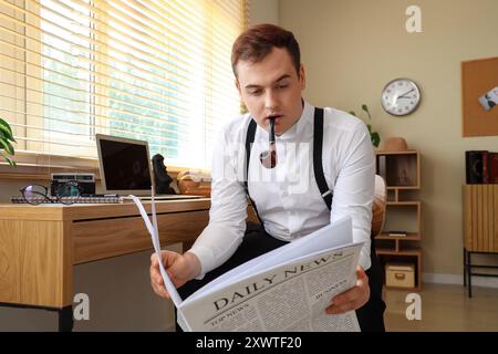 Männlicher Detektiv mit Rauchpfeife, der Zeitung am Tisch im Büro liest Stockfoto