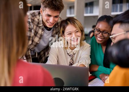 Eine Gruppe von verschiedenen, lächelnden jungen Studenten, die sich mit einem Laptop im Klassenzimmer der Universität versammeln. Stockfoto