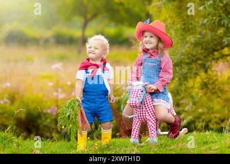 Kleiner Junge und Mädchen verkleidet als Cowboy und Cowgirl, die im Park mit Spielzeug schaukelndem Pferd spielen. Kinder spielen im Freien. Kinder in Halloween-Kostümen Stockfoto