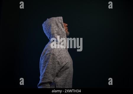 Porträt eines mysteriösen Mannes mit Kapuzenpullover, der still steht. Isoliert auf dunklem Hintergrund. Stockfoto