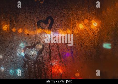 Herzen gezeichnet auf einem regenbedeckten Fenster mit bunten Bokeh-Lichtern im unscharfen Hintergrund, romantische und stimmungsvolle Atmosphäre Stockfoto