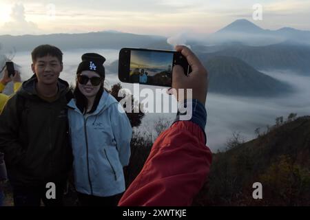 Ein Pärchen lässt sich bei Sonnenaufgang vor dem Tengger-Caldera fotografieren. Im Hintergrund ist der Vulkan Semeru, mit 3676 m Höhe der höchste Berg der indonesischen Insel Java, zu sehen. Der Nationalpark Bromo-Tengger-Semeru besteht seit 1982. Der mittlere Teil des Namens verweist auf das hier lebende Volk der Tengger. Zum Nationalpark gehören der 3676 m hohe Stratovulkan Semeru, der höchste Berg der Insel, sowie vier in der Tengger-Caldera liegende Vulkane, deren Bekanntester der Bromo ist. Die Caldera wird vom Tengger-Sandmeer malaiisch: Laut Pasir Tengger ausgefüllt. Vier gesehen und etwa Stockfoto