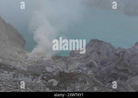 Eingekreist von einer zerfurchten Felswand liegt im Krater des Gunung Iljen der Kratersee. Seine grünlich-blaue Farbe ist auf hohe Konzentrationen von Alaun, Schwefel und Gips zurückzuführen. Mit einem pH-Wert um 0,3 und seiner wird er als größtes Säurefass der Erde bezeichnet. Kratersee - Breite: 600 m - Länge: 960 m - Tiefe: bis zu 200 m *** umringt von einer gefurchten Felswände liegt der Kratersee im Krater von Gunung Iljen seine grünlich-blaue Farbe ist auf hohe Konzentrationen von Alaun, Schwefel und Gips mit einem pH-Wert von etwa 0,3 zurückzuführen, es ist bekannt als das größte Säurefass der Erde Crate Stockfoto