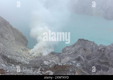 Eingekreist von einer zerfurchten Felswand liegt im Krater des Gunung Iljen der Kratersee. Seine grünlich-blaue Farbe ist auf hohe Konzentrationen von Alaun, Schwefel und Gips zurückzuführen. Mit einem pH-Wert um 0,3 und seiner wird er als größtes Säurefass der Erde bezeichnet. Kratersee - Breite: 600 m - Länge: 960 m - Tiefe: bis zu 200 m *** umringt von einer gefurchten Felswände liegt der Kratersee im Krater von Gunung Iljen seine grünlich-blaue Farbe ist auf hohe Konzentrationen von Alaun, Schwefel und Gips mit einem pH-Wert von etwa 0,3 zurückzuführen, es ist bekannt als das größte Säurefass der Erde Crate Stockfoto