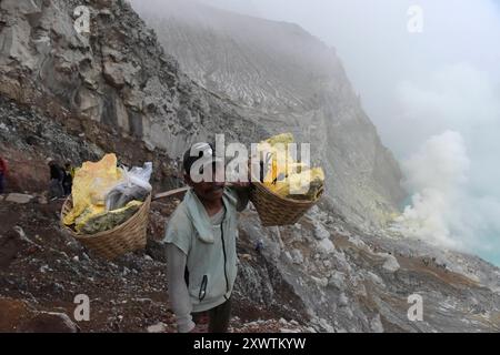 Eingekreist von einer zerfurchten Felswand liegt im Krater des Gunung Iljen der Kratersee. Seine grünlich-blaue Farbe ist auf hohe Konzentrationen von Alaun, Schwefel und Gips zurückzuführen. Mit einem pH-Wert um 0,3 und seiner wird er als größtes Säurefass der Erde bezeichnet. Seit der Kolonialzeit wird an so genannten Solfataren am Südostufer des Kratersees Schwefel abgebaut. Keramikrohre leitet das oxidierende mit Wasserdampf vermischte Gas von der Austrittsstelle weg, wodurch es abkühlt, sich anreichert und in gelben Brocken abtransportiert wird. Arbeiter tragen dreimal täglich bis zu 90 kg Stockfoto