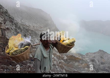 Eingekreist von einer zerfurchten Felswand liegt im Krater des Gunung Iljen der Kratersee. Seine grünlich-blaue Farbe ist auf hohe Konzentrationen von Alaun, Schwefel und Gips zurückzuführen. Mit einem pH-Wert um 0,3 und seiner wird er als größtes Säurefass der Erde bezeichnet. Seit der Kolonialzeit wird an so genannten Solfataren am Südostufer des Kratersees Schwefel abgebaut. Keramikrohre leitet das oxidierende mit Wasserdampf vermischte Gas von der Austrittsstelle weg, wodurch es abkühlt, sich anreichert und in gelben Brocken abtransportiert wird. Arbeiter tragen dreimal täglich bis zu 90 kg Stockfoto