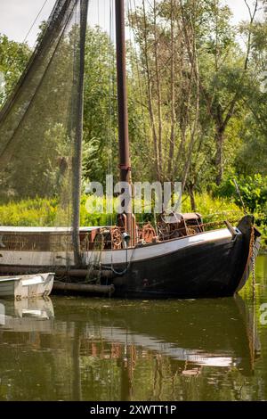 Ein Fischerboot mit einem großen Netz liegt auf ruhigem Wasser und spiegelt an klaren Tagen Bäume vom Ufer. Stockfoto