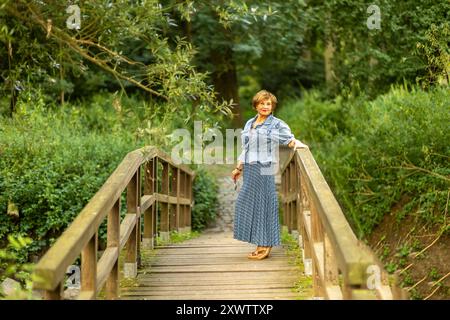 Eine Frau posiert anmutig auf einer Brücke, mit lebendigem Laub im Hintergrund und genießt einen friedlichen Moment in der Natur. Stockfoto