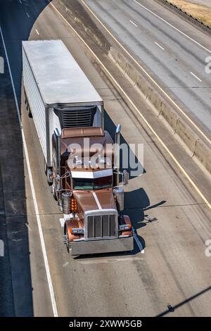 Klassischer brauner Sattelzugmaschine mit großem Lkw mit verlängerter Fahrerkabine und Chromteilen für Lkw-Fahrer, die Ladung im Kühlauflieger transportieren Stockfoto