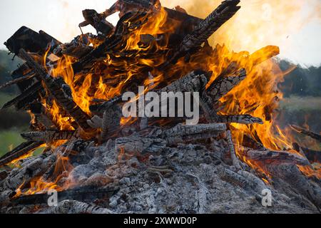 Aus nächster Nähe sehen Sie ein Lagerfeuer mit brennendem Holz, das intensive Flammen und verkohlte Baumstämme in einer Umgebung im Freien zeigt. Es fängt einen warmen, dramatischen geldautomaten ein Stockfoto