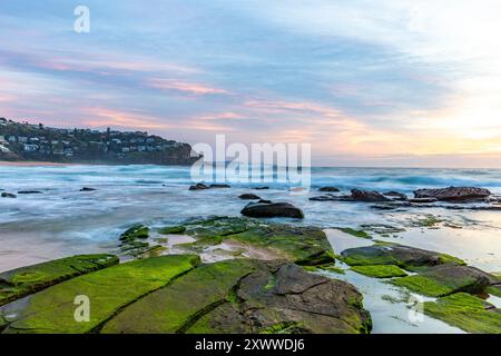 Sydney Sonnenaufgang über Whale Beach, orange roter Himmel mit grünen Algen auf Felsen am Wasser, NSW, Australien Stockfoto