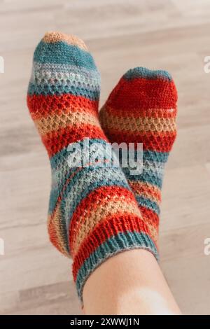 Farbenfrohe Stricksocken an den Füßen der Frau. Helle Wollsocken mit Streifen. Warme Kleidung für den späten Herbst. Kuschelige Strickmode. Handgefertigte Kleidung Stockfoto